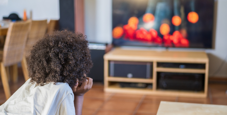 A boy with curly dark hair looks at a television across the room.