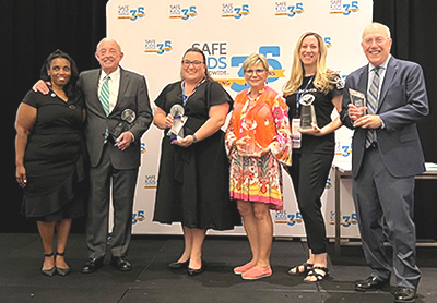 Six people stand on stage holding awards at convention.