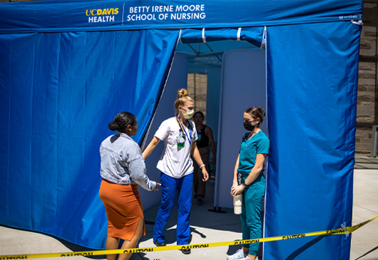 Nursing student in scrubs exits emergency tent while nurse and evacuee wait outside