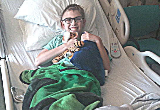 James in his hospital bed, holding stuffed animal and pillow
