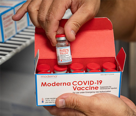Pair of hands holding Moderna vaccine vile and box.