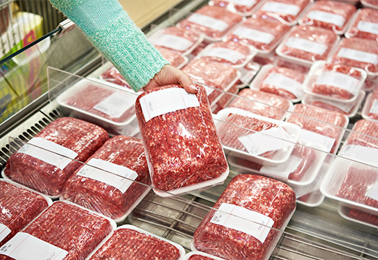 Ground beef packs in grocery store, with a woman&#x2019;s hand reaching for a packet and picking it up.