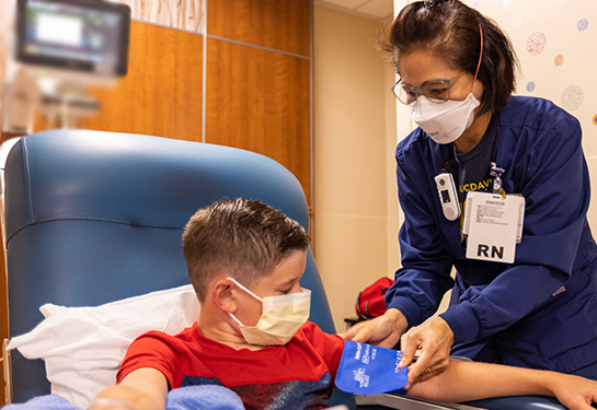 Nurse wearing mask and blue scrubs putting blood pressure cuff on child’s arm