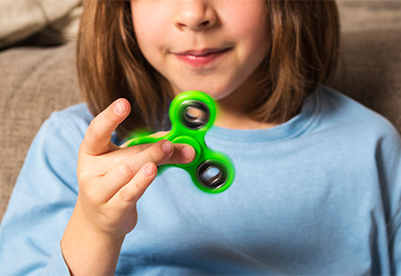 A child, whose face is not fully visible, uses a bright green fidget spinner. 
