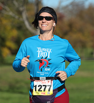 Blonde woman with blue shirt that reads Davis Turkey Trot and red pants running with the race number 1277 pinned to shirt.