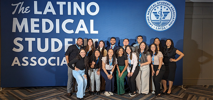 A group of 15 medical students stand before a large blue background that states, “The Latino Medical Student Association.”