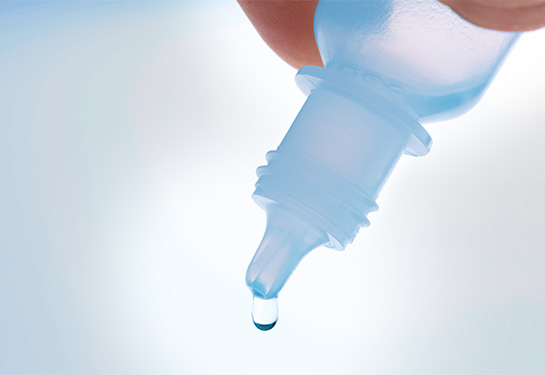 Close-up of eye drop bottle showing a drip with a white background