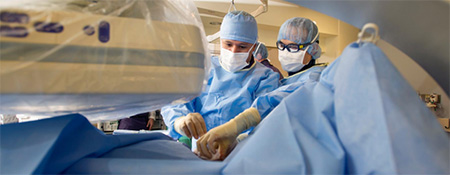 Dr. Godoy and another person wearing blue scrubs, masks and head cover while operating in the theater of an operating room.