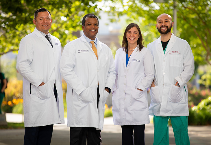 Group of four people outdoors wearing white coats and smiling into camera.