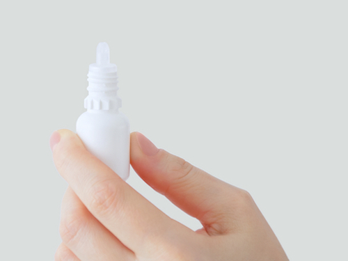 A hand holds a white eyedrop bottle against a light grey background. 