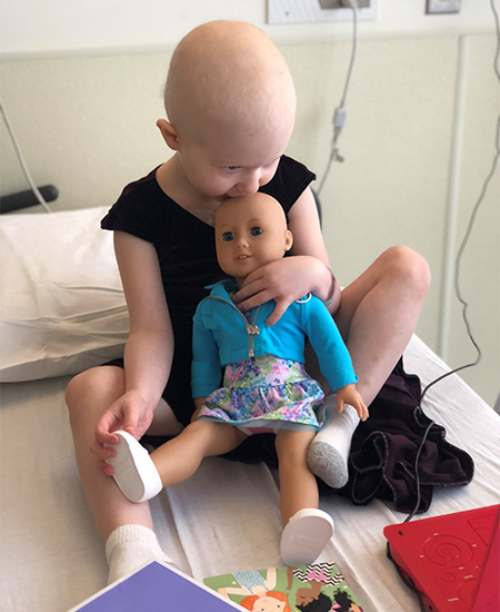 Hairless child playing with a hairless doll sitting on a hospital bed