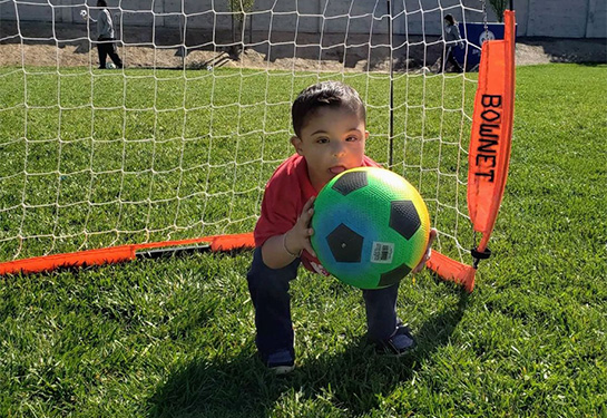 A young boy catches a soccer ball with the goal behind him.