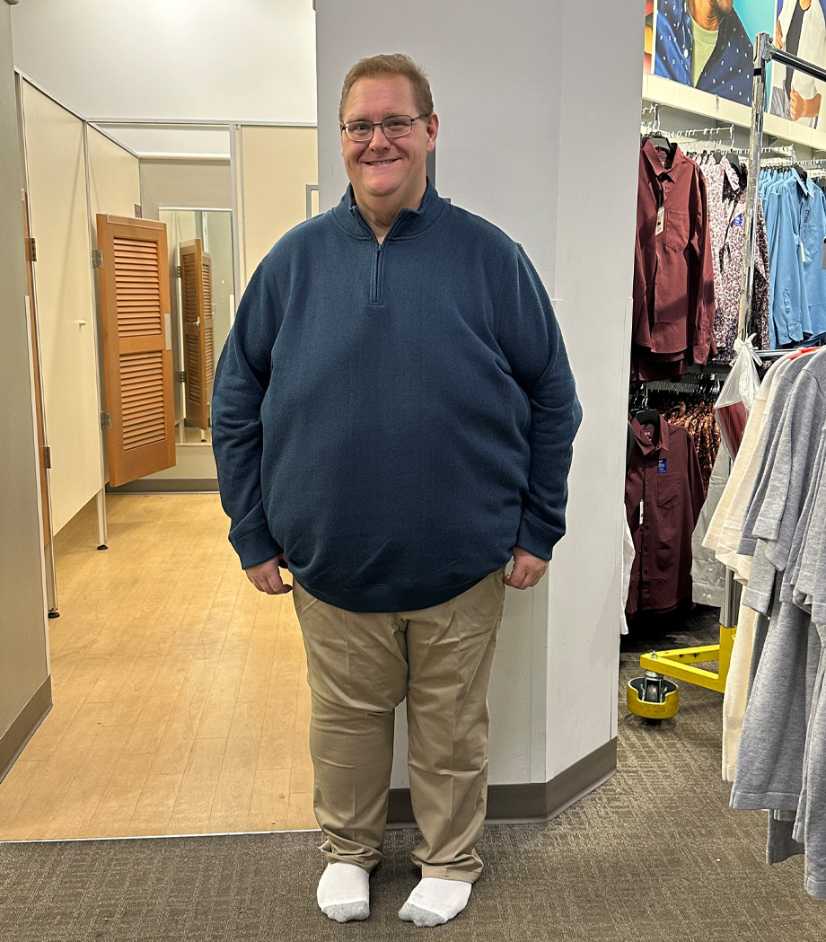 Man in blue pullover sweater, khaki pants and white socks stands outside department store dressing room