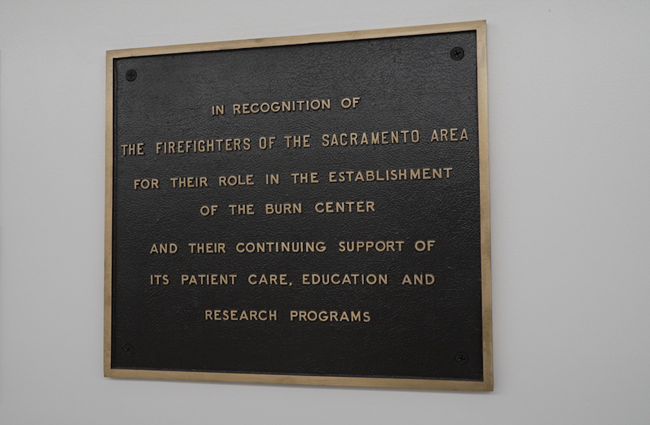 Wall plaque with black background and bronze lettering recognizes Sacramento area firefighters for establishing the burn center.