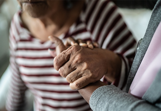 A close-up photo shows a caregiver holding the hand of a senior woman in a striped shirt.
