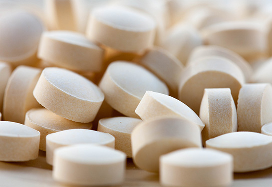 A close-up view of a pile of cream-colored round pills on a flat surface.