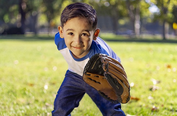 Boy wearing blue baseball shirt, jeans and a mitt stands in a grassy field. 