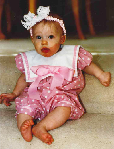 A baby wearing a pink and white polka dot outfit and pink headband. 