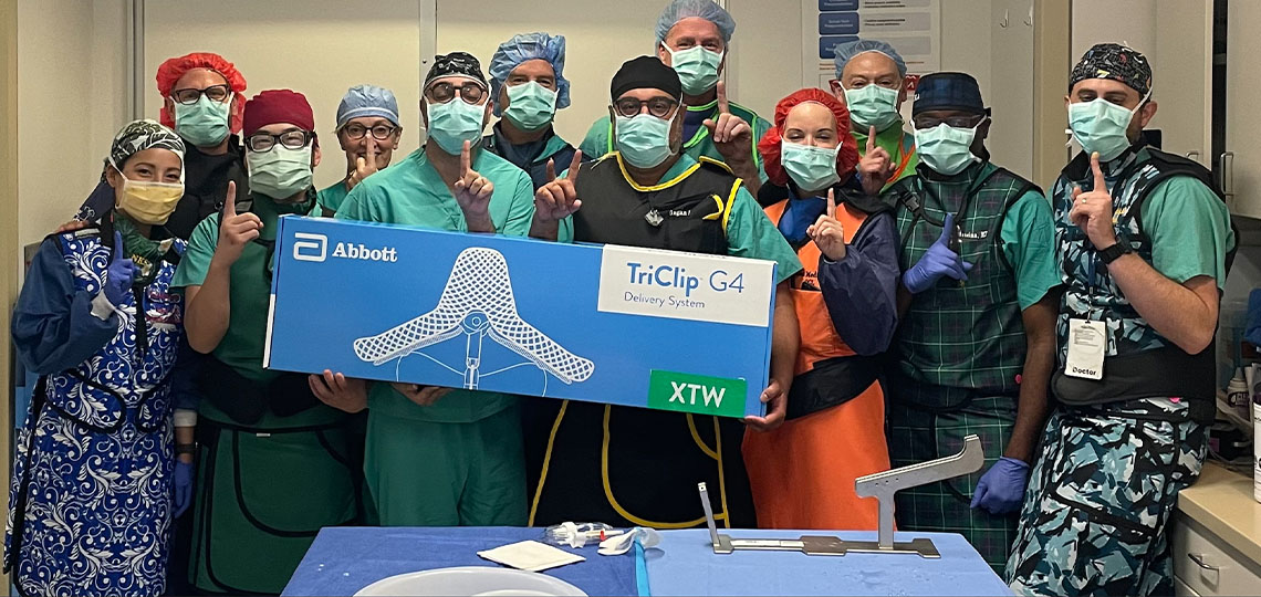 Group of people wearing surgical masks and PPE standing together with people in front holding box that says Abbott TriClip G4 System.