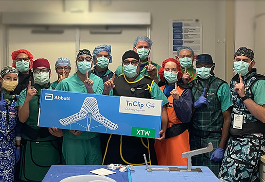 Group of people wearing surgical masks and PPE standing together with people in front holding box that says Abbott TriClip G4 System.