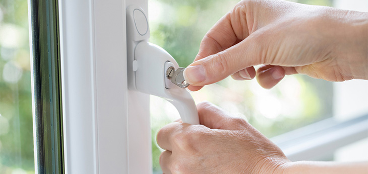 Hand of person using key to lock window handle 