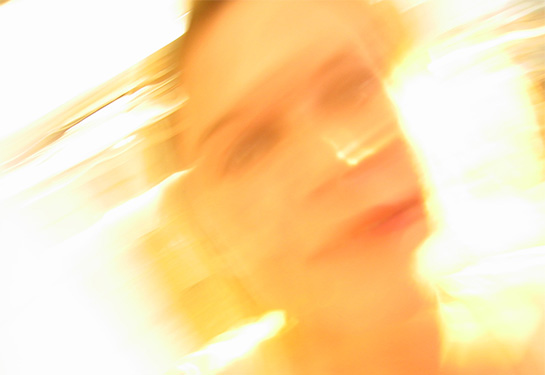 A distorted photo of a woman’s face against a bright background. 
