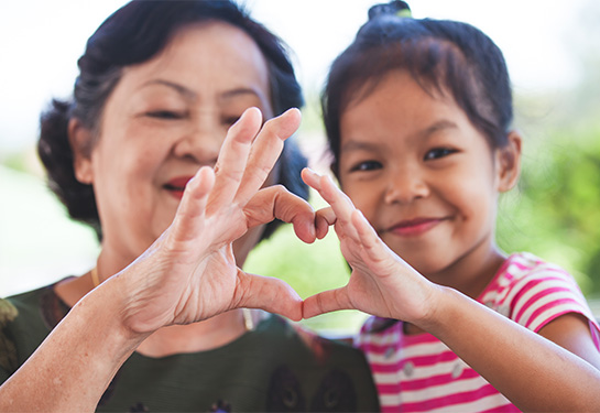A senior Vietnamese grandmother with her granddaughter making a heart shape with their hands