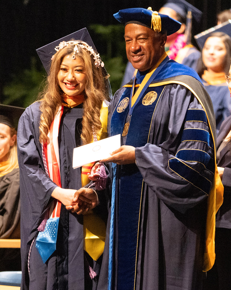 Chancellor Gary May, right, holds graduate certificate in hand while shaking hand with female graduate