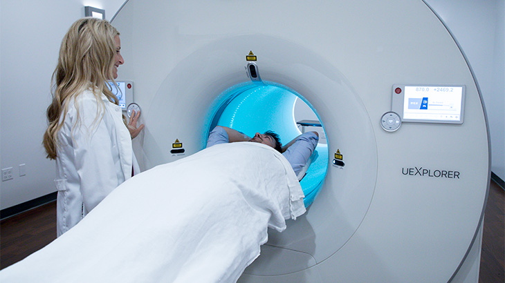 Patient entering advanced PET scanner EXPLORER with woman in white coat smiling at him.