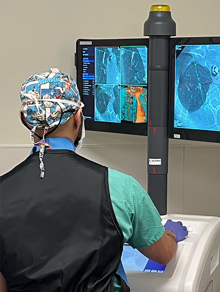 View of the back of a man in scrubs looking at images of lungs on a monitor