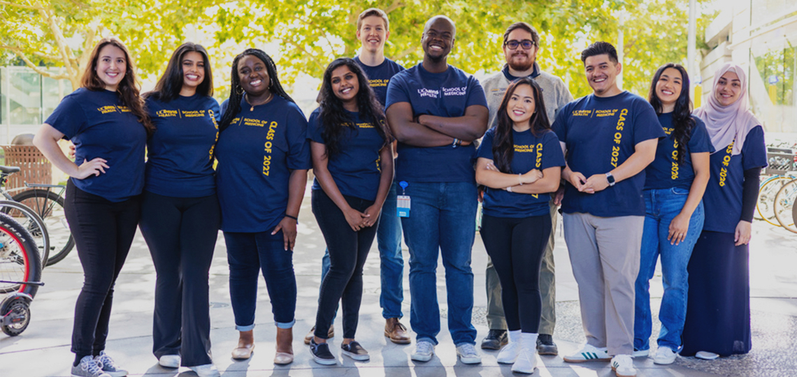 A diverse group of 12 medical students stand shoulder-to-shoulder wearing blue UC Davis t-shirts