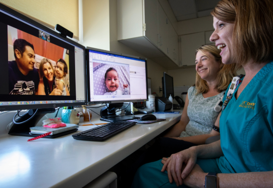 Young child with parents on video on computer screen speaking to nurse wearing teal scrubs and another person  