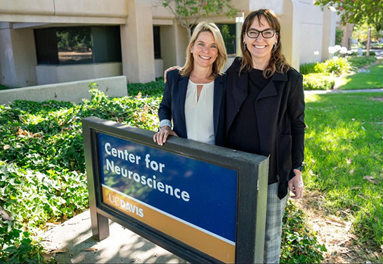 Two women stand behind a sign for the UC Davis Center for Neuroscience