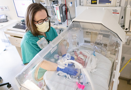 Doctor looks at baby in isolette in NICU