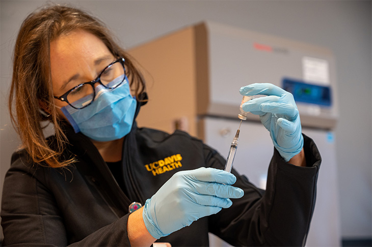 A nurse wearing a blue mask fills a needle with vaccine.