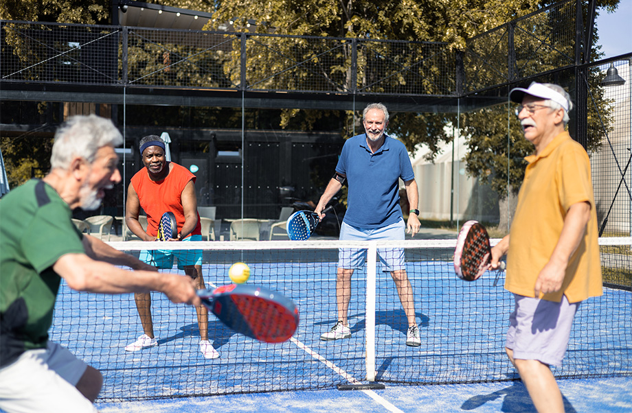 A group of four adults plays pickleball on a blue court outside. 