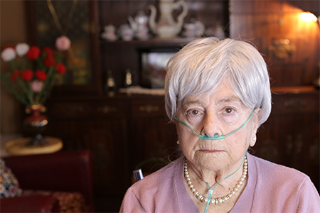 Older woman sitting in chair with green oxygen tubes going into her nostrils