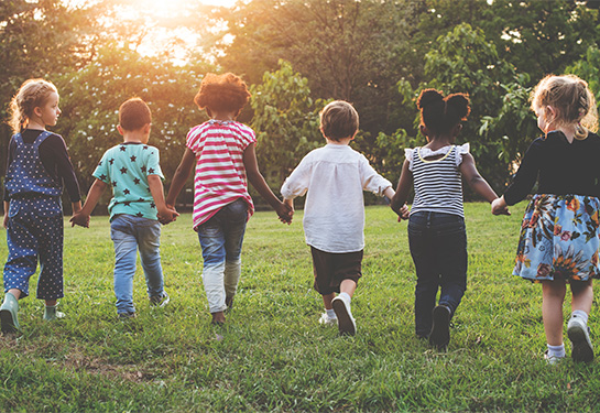 A diverse group of young children run across a field while holding hands. 