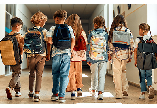 7 children standing side by side wearing backpacks in school hallway