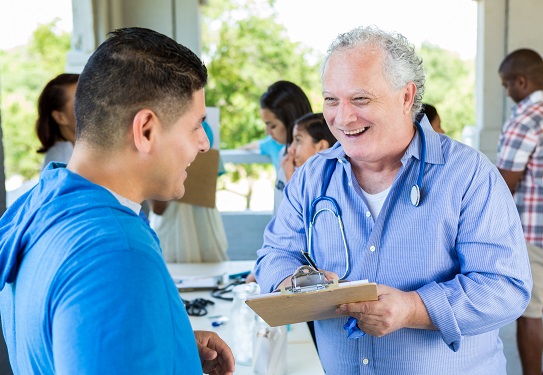 A man with a stethocope around neck greets a patient