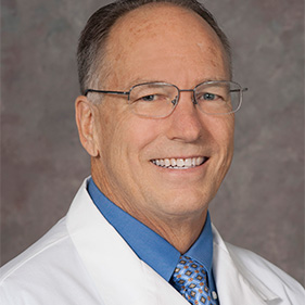 A man with brown hair in a white medical coat smiles