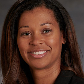 Woman with dark, brown hair wearing a white coat and smiling into camera.