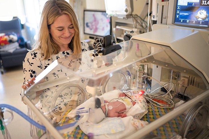 Woman looks over baby in NICU isolette.