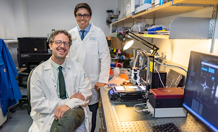 Two men smiling into the camera with a lab in the background.