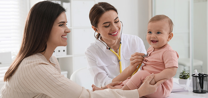 Female doctor examining baby while female looks on