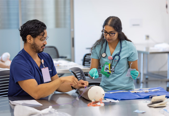 Nursing instructor, left, holds manikin arm while student practices starting IV