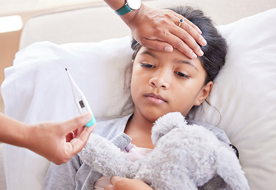 Little girl has her temperature taken with a thermometer by a parent at home