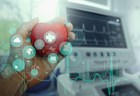 A hand holds a model of a heart in front of medical device’s digital screen