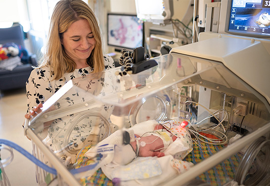 Woman looks over baby in NICU isolette.