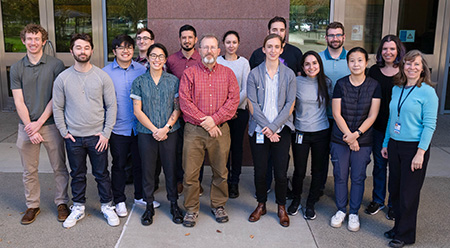 A photo of Professor Andreas Bäumler with 14 members of his lab standing in front of a building.